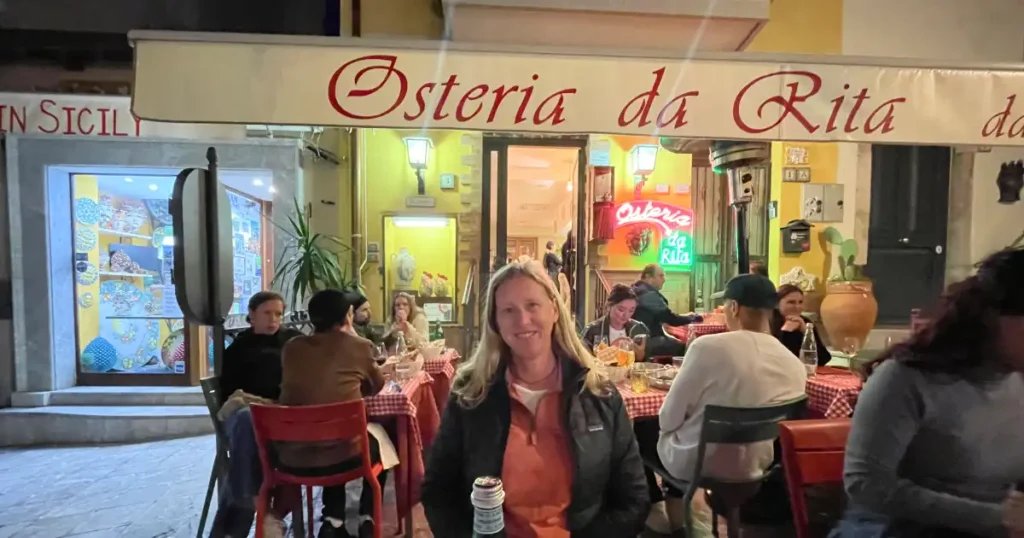 Meghan is sitting in front of Osteria da Rita in Taormina